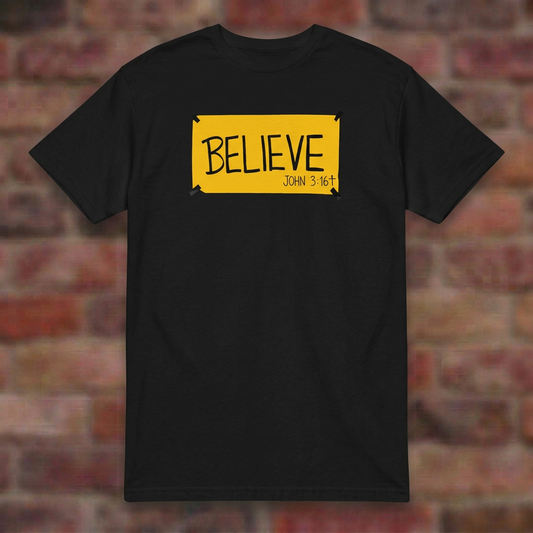 BELIEVE John 3:16 Black T-shirt flat lay on softly blurred bricks