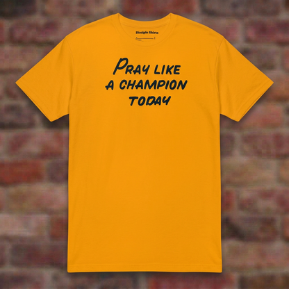 Pray Like a Champion T-shirt in Gold, flat lay on blurred brick