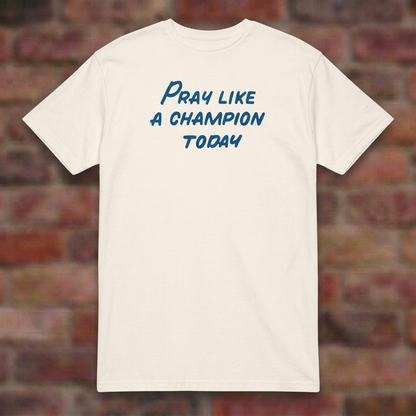 Pray Like a Champion T-shirt in Natural, flat lay on blurred brick