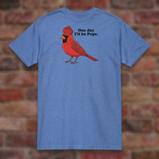 One day I'll be Pope T-shirt in Heather Royal, flat lay on blurred brick
